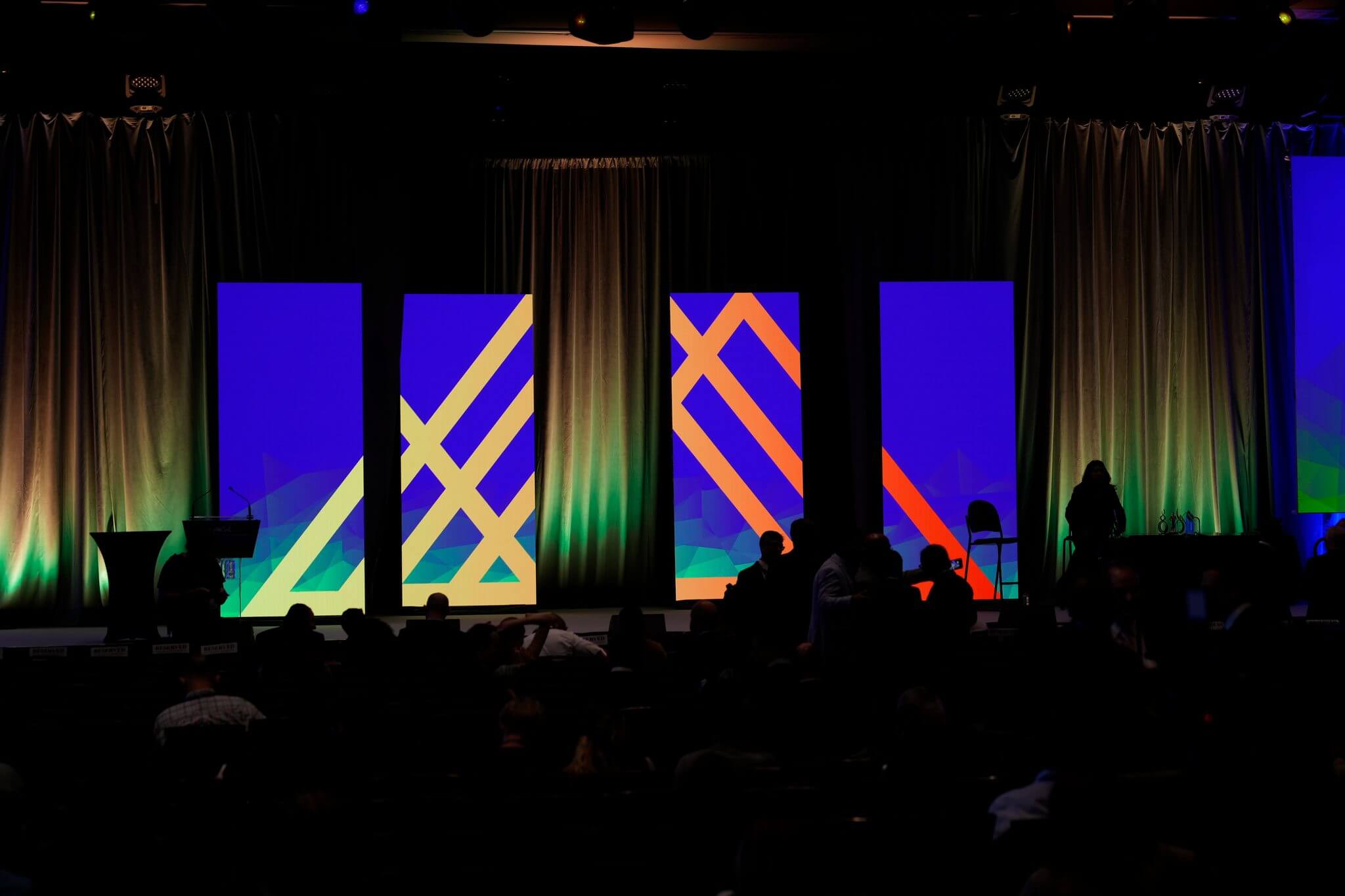A dark room at a live event with a colorful graphic on the screen.